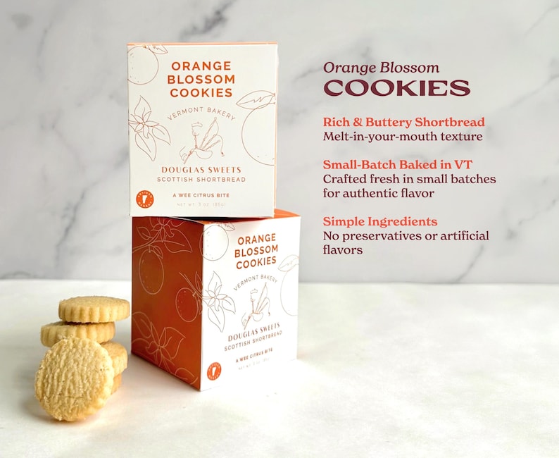 a box of Vermont Bakery's Orange Blossom Cookies, with a stack of cookies placed next to it. The box is orange and white, and the cookies are white.
