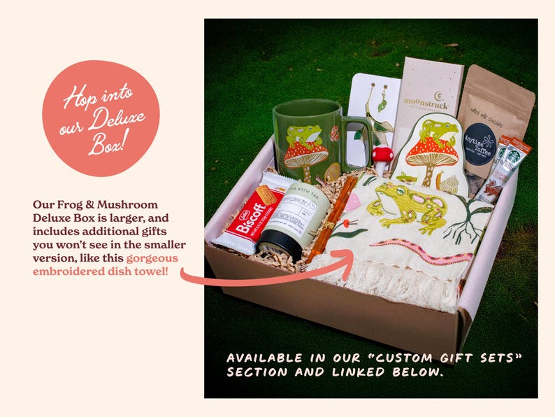 Expanded deluxe version of the frog and mushroom themed gift set displayed on a forest green background. Includes an embroidered dish towel alongside the mug trinket tray jasmine green tea and snacks. Designed for thoughtful gifting and relaxing woodland-inspired afternoons.