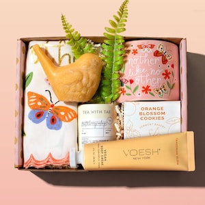 A gift box with a variety of items, including a bird-shaped soap, a floral-decorated mug with the text "mother like no other", a hand towel with a butterfly design, a candle, cookies, and a tangerine-scented body cream.