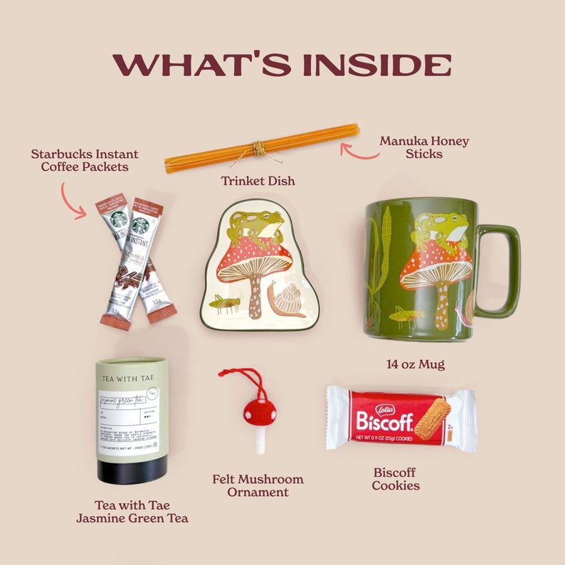 Flat lay of all items included in the toad-ally charming gift set showing the green frog and mushroom mug matching trinket dish jasmine green tea tin manuka honey sticks biscoff cookies and red felt mushroom ornament. An inviting overview of this delightful woodland tea and treat collection.