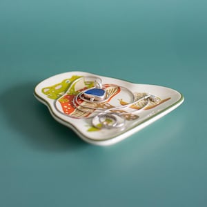 Detailed photo of the ceramic frog and mushroom trinket dish holding small accessories on a pastel surface. Adorned with woodland toadstool art this dish adds charm to nightstands and vanities perfect for jewelry tea bags or tiny keepsakes.