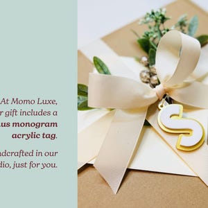 A gift box with a ribbon and a monogram acrylic tag, along with a small gold letter 'S' charm.