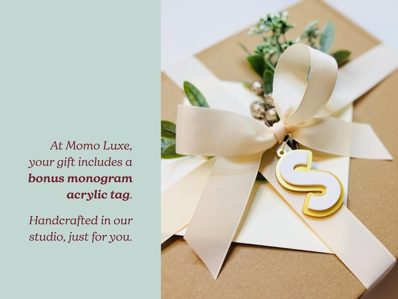 A gift box with a ribbon and a monogram acrylic tag, along with a small gold letter 'S' charm.