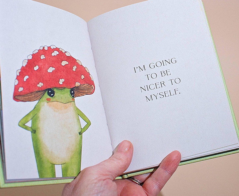 An open page from the self-care book showing a colorful watercolor illustration of a frog wearing a red mushroom cap next to the text, 'I'm going to be nice to myself.'