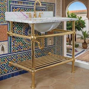Puede incluir: Un lavabo de baño de metal dorado con una encimera de mármol blanco y un lavabo de porcelana blanca. El lavabo tiene un grifo y accesorios dorados. El marco es de metal dorado con una balda inferior. El fondo presenta una pared de azulejos de mosaico coloridos.