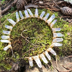 May include: A gold wire headband with clear quartz crystals wrapped around it. The headband is on a bed of moss.