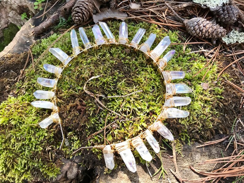 May include: A gold wire headband with clear quartz crystals wrapped around it. The headband is on a bed of moss.