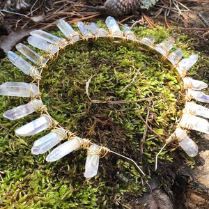 May include: A gold wire headband with clear quartz crystals attached. The headband is on a bed of green moss.