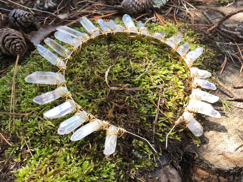 May include: A gold wire headband with clear quartz crystals attached. The headband is on a bed of green moss.