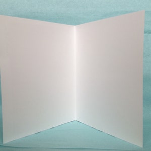May include: A blank white card folded in half, ready for writing or decorating. The card is on a light blue background.