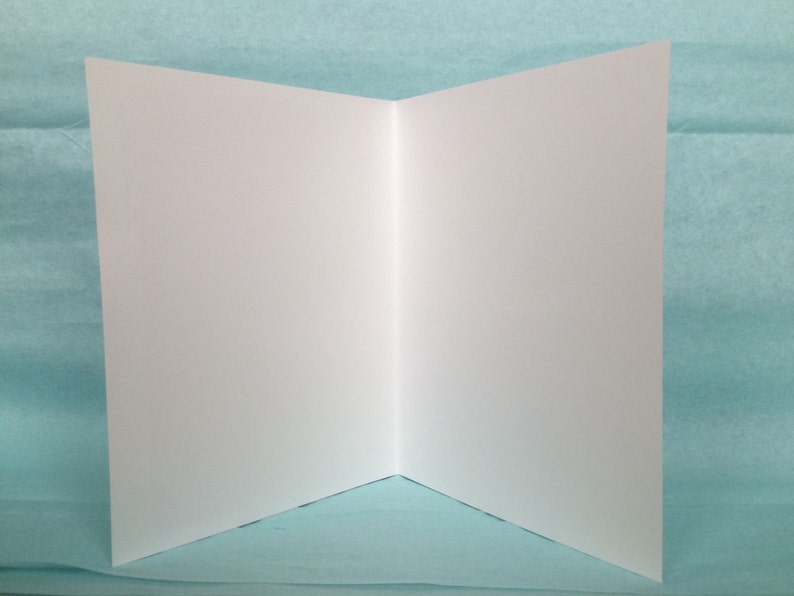 May include: A blank white card folded in half, ready for writing or decorating. The card is on a light blue background.