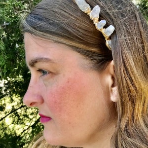 May include: A gold wire headband with clear quartz crystals attached. The headband is worn by a person with long blonde hair.