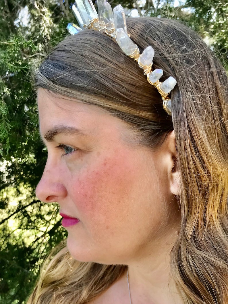May include: A gold wire headband with clear quartz crystals attached. The headband is worn by a person with long blonde hair.