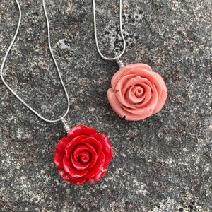 May include: Two silver chain necklaces with rose-shaped pendants. One pendant is a light pink rose, the other is a bright red rose.