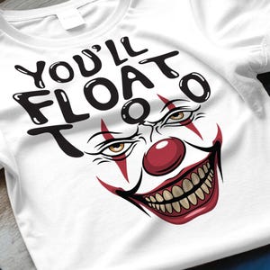 Puede incluir: Camiseta blanca con un diseño de cara de payaso aterrador y el texto "YOU'LL FLOAT TOO" en negro. El payaso tiene una nariz roja, una amplia sonrisa y ojos amarillos. La camiseta está hecha de un material suave.