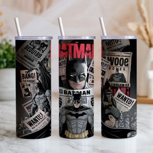 May include: Three black Batman-themed tumblers with white straws. Each tumbler features a different Batman graphic, with the word "Batman" in red. The design includes comic book-style elements and the words "WANTED!" and "BANG!"