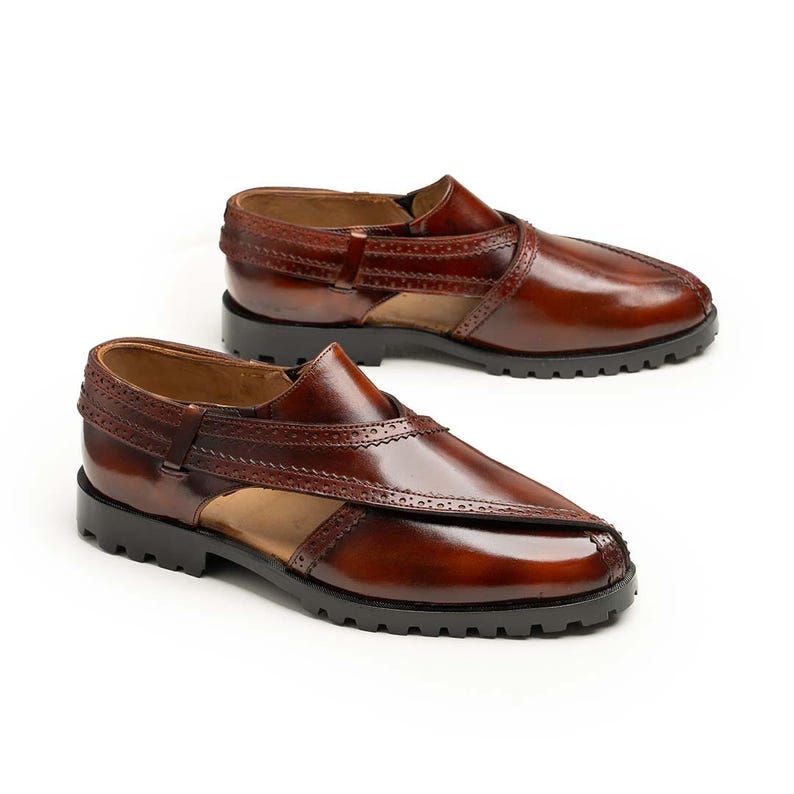 May include: A pair of brown leather sandals with a glossy finish. The sandals have a unique design with cut-out sections and decorative stitching. They have a sturdy black sole and a classic, elegant style.