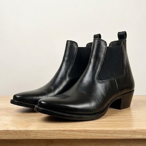 Puede incluir: Un par de botines Chelsea de cuero negro con acabado liso, puntera puntiaguda, paneles laterales elásticos y tacón bajo de bloque. Cada bota incluye una pequeña lengüeta en la parte posterior del tobillo, ofreciendo un diseño elegante.