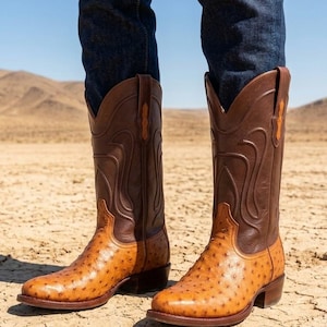 Op de afbeelding: Een paar western-cowboylaarzen met een lichtbruine voorvoet van struisvogelleder met een opvallend veerpatroon en een donkerbruine schacht van leder met decoratieve stiksels. De laarzen hebben een spitse neus en een lage, gestapelde blokhak.