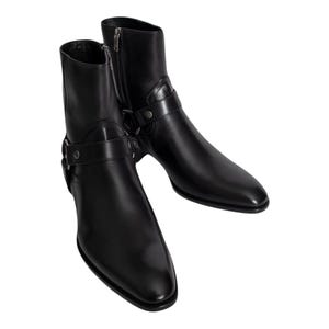 May include: A pair of black leather ankle boots with a pointed toe and a side zip. Each boot features a strap with a buckle and a metal ring detail. The boots are designed for a sleek, modern look.