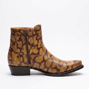 May include: An ankle boot featuring a brown and yellow snakeskin pattern, a side zipper closure, a pointed toe, and a dark brown stacked heel. The boot has a structured silhouette with visible stitching along the side panel and a smooth finish.