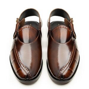 May include: A pair of brown leather Peshawari sandals. These open-toe shoes feature a slingback strap with a buckle closure and decorative stitching along the vamp. The sandals have a glossy finish and a dark sole.