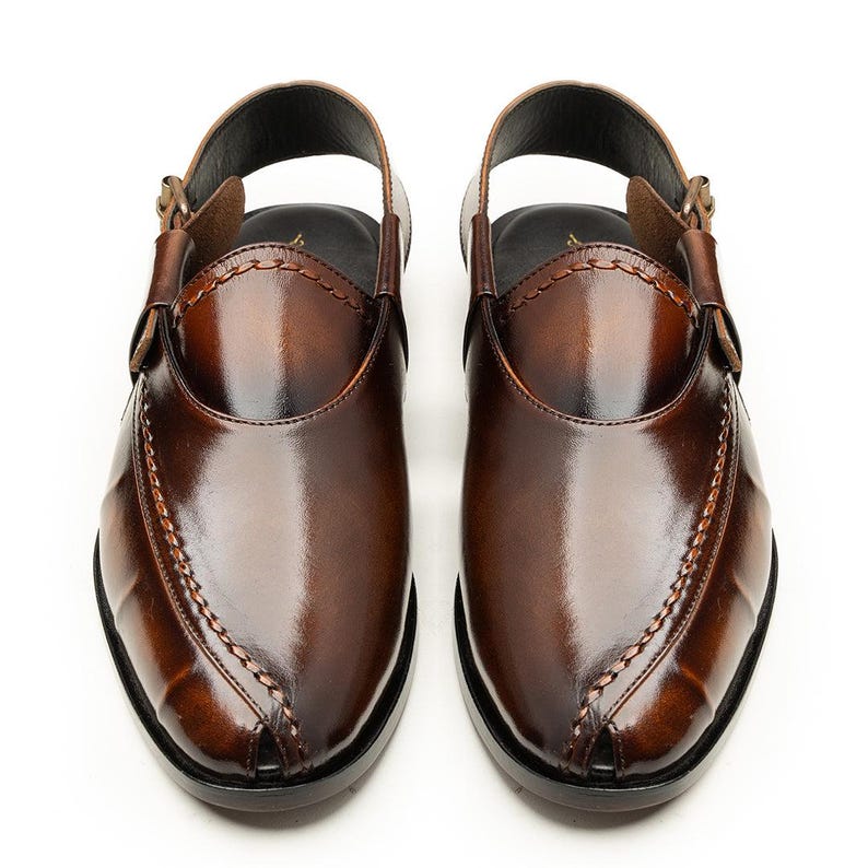 May include: A pair of brown leather Peshawari sandals. These open-toe shoes feature a slingback strap with a buckle closure and decorative stitching along the vamp. The sandals have a glossy finish and a dark sole.