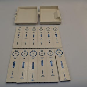 May include: A set of twelve off-white rectangular sewing machine pattern cams with blue printed icons and numerical labels, accompanied by two matching off-white plastic storage cases. Each cam features distinct stitch diagrams and numbers.