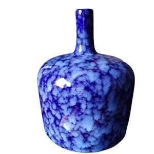 May include: A ceramic vase with a bulbous body and a narrow, cylindrical neck. The surface features a mottled, crystalline glaze pattern in shades of deep royal blue and lighter, icy blue, creating a textured, cloud-like appearance throughout.