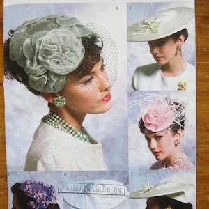 Peut inclure: Patron Vogue Accessoires présentant différents chapeaux vintage. L'image montre un grand chapeau gris fleuri avec un voile, un chapeau blanc avec un nœud, et un chapeau rose fleuri. Le patron est étiqueté V8052.