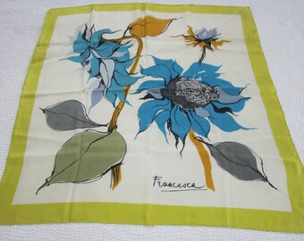 Könnte beinhalten: Ein weißer Seidenschal mit gelbem Rand zeigt ein blaues und grünes Blumenmuster. Die Blumen sind stilisierte Sonnenblumen mit schwarzem Zentrum. Der Schal ist unten rechts mit "Francesca" signiert.
