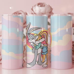 Op de afbeelding: Drie roestvrijstalen bekers met een pastelkleurig wolkenontwerp. De middelste beker toont Bugs Bunny en Lola Bunny die elkaar omhelzen in een hartvormig ontwerp. De andere twee bekers hebben een vergelijkbaar pastelkleurig wolkenontwerp.