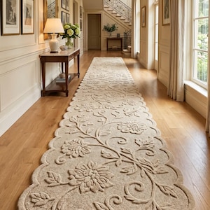 May include: Beige floral runner rug with a scalloped edge. The rug features a repeating pattern of large flowers and leaves. The rug is placed in a hallway with hardwood floors and framed artwork.