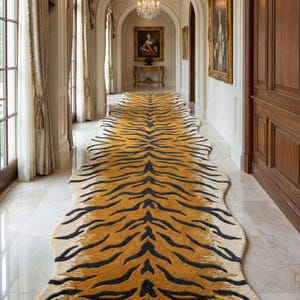 May include: A long, rectangular rug with a tiger stripe pattern in shades of tan, black, and cream. The rug is placed in a hallway with marble flooring, ornate chandeliers, and framed artwork. The rug's dimensions are approximately 10 feet long.