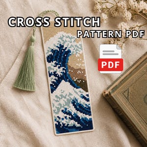 May include: A rectangular cross stitch bookmark featuring a stylized ocean wave design in shades of blue, white, and tan. The bookmark includes a sage green tassel attached to the top and displays the text CROSS STITCH PATTERN PDF.