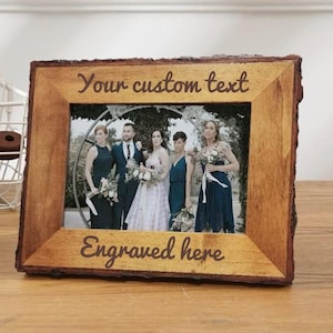May include: Wooden picture frame with a natural bark edge, displaying a wedding photo. The frame has the text "Your custom text" at the top and "Engraved here" at the bottom. The frame is sitting on a wooden surface.