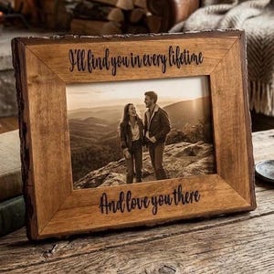 May include: A rectangular wooden picture frame with a natural live edge, featuring the engraved text "I'll find you in every lifetime" at the top and "And love you there" at the bottom, containing a photograph of two people standing on a mountain.