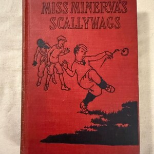 Peut inclure: Un livre ancien à couverture rigide rouge intitulé "Miss Minerva's Scallywags". La couverture présente des illustrations d'enfants en noir et blanc, dont un en pleine action. La tranche du livre est visible.