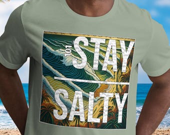 May include: Sage green t-shirt featuring the text "STAY SALTY" in white. The graphic is a tropical beach scene with palm trees and ocean waves. The short-sleeved shirt is made of a soft material.