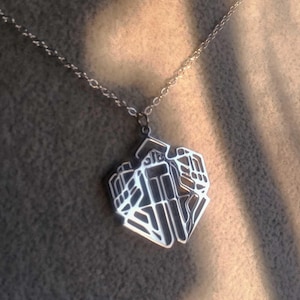 May include: Silver pendant necklace with a geometric design. The pendant has a detailed, openwork pattern, suspended from a delicate chain. The necklace is displayed on a neutral surface, with soft lighting.