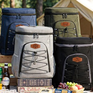 Può includere: Una collezione di zaini frigo isolanti in blu navy, verde oliva, grigio e nero. Ogni zaino ha una cerniera superiore, una tasca frontale e dettagli in corda. Ideali per picnic e gite.