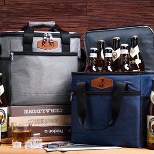 May include: A grey cooler bag with an RM leather patch and a navy blue cooler bag with a James leather patch, both featuring black handles and zips. Several brown glass beer bottles with labels including Vedett and Franziskaner are present.