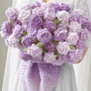 May include: A handmade crochet bouquet featuring fluffy, textured flowers in shades of lavender and pale pink. The flowers are arranged with green accents and held in a matching lavender crochet wrap.