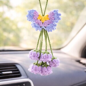 Puede incluir: Un adorno de coche hecho a mano con ganchillo, con un dise&ntilde;o de mariposa en tonos azules, morados y amarillos. Debajo de la mariposa, hay acentos en forma de flor de lavanda, suspendidos por cuerdas verdes. Este art&iacute;culo decorativo cuelga del espejo retrovisor.