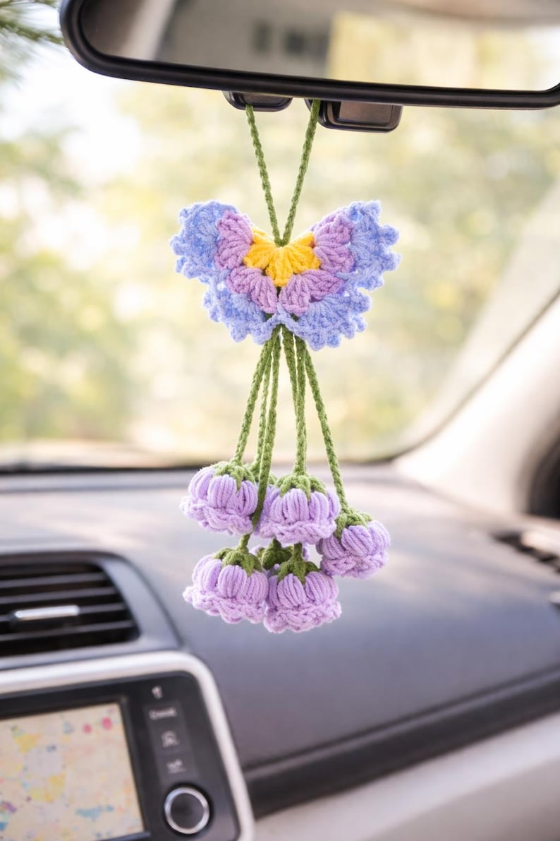 Puede incluir: Un adorno de coche hecho a mano con ganchillo, con un dise&ntilde;o de mariposa en tonos azules, morados y amarillos. Debajo de la mariposa, hay acentos en forma de flor de lavanda, suspendidos por cuerdas verdes. Este art&iacute;culo decorativo cuelga del espejo retrovisor.