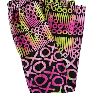 May include: Black patterned trousers featuring pink, yellow, and black shapes. The design includes circles, lines, and X's and O's. The trousers are folded, showing the elasticated waistband.