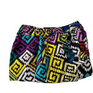 May include: A colorful, patterned clutch bag. The bag features a repeating geometric design in black, white, yellow, purple, teal, and red. The bag is gathered at the top and appears to be made of a lightweight fabric.
