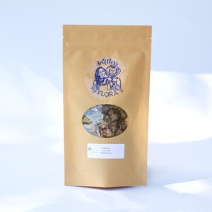 May include: A brown paper pouch with a clear oval window revealing dried plant matter inside. The pouch features a circular blue logo with the text Driftless Flora and a white rectangular label reading Wild Rose, 1 oz for $6, 2025 Harvest.