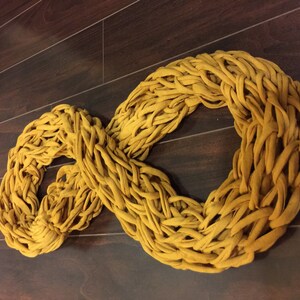 May include: A mustard yellow chunky knit infinity scarf made from a soft, stretchy fabric.
