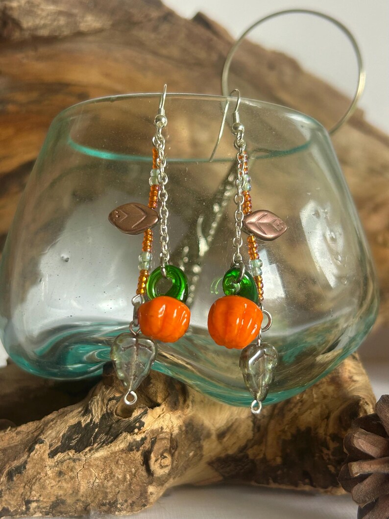 Peut inclure: Boucles d'oreilles faites &agrave; la main avec des perles de citrouille orange, des anneaux en verre vert et des breloques en forme de feuille. Les boucles d'oreilles ont des crochets et des cha&icirc;nes de couleur argent&eacute;e, avec des accents de perles orange et vertes.